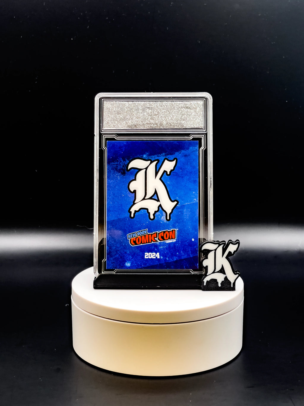 Collectible card with 'K' logo on a stand against a black background
